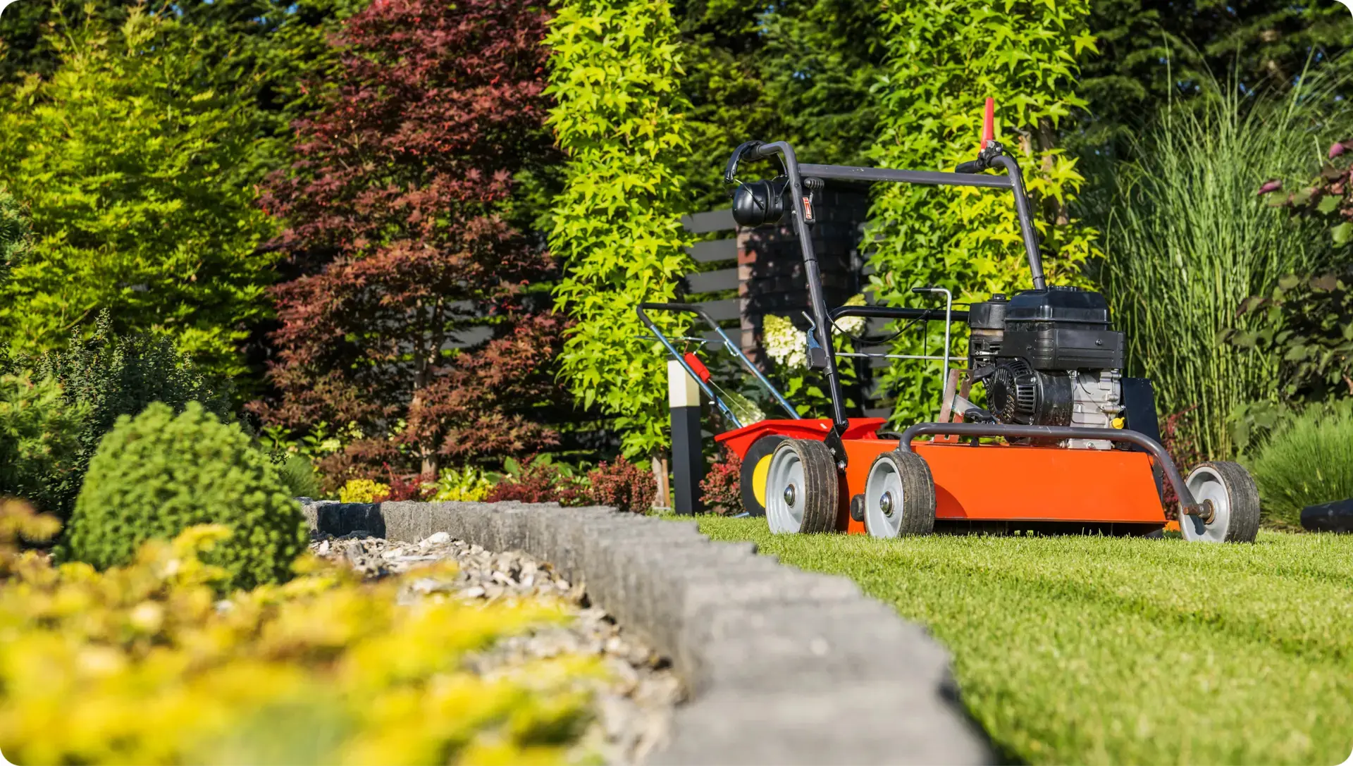 Lawn mower on green grass near garden.